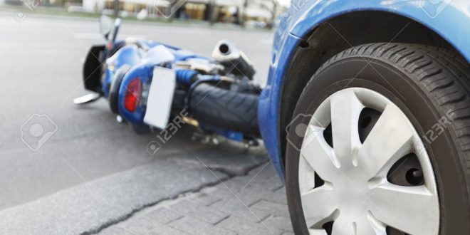 The accident blue bike with a blue car. The motorcycle crashed into the bumper of the car on the road. The motorcycle lies on the road near the car.